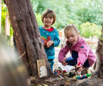 Two Nursery children playing next to tree