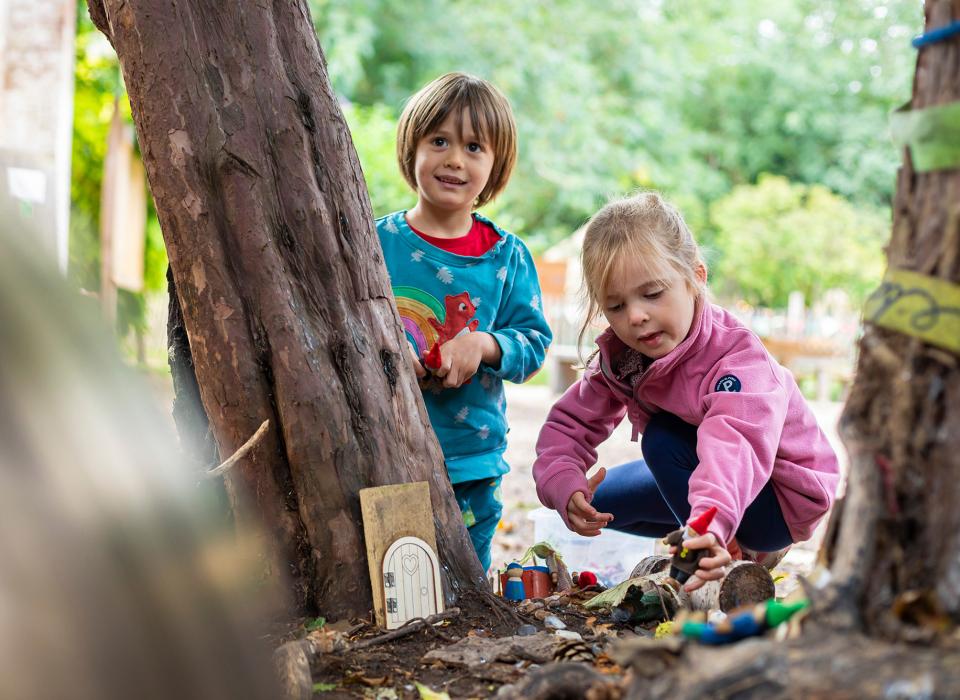 Two Nursery children playing next to tree